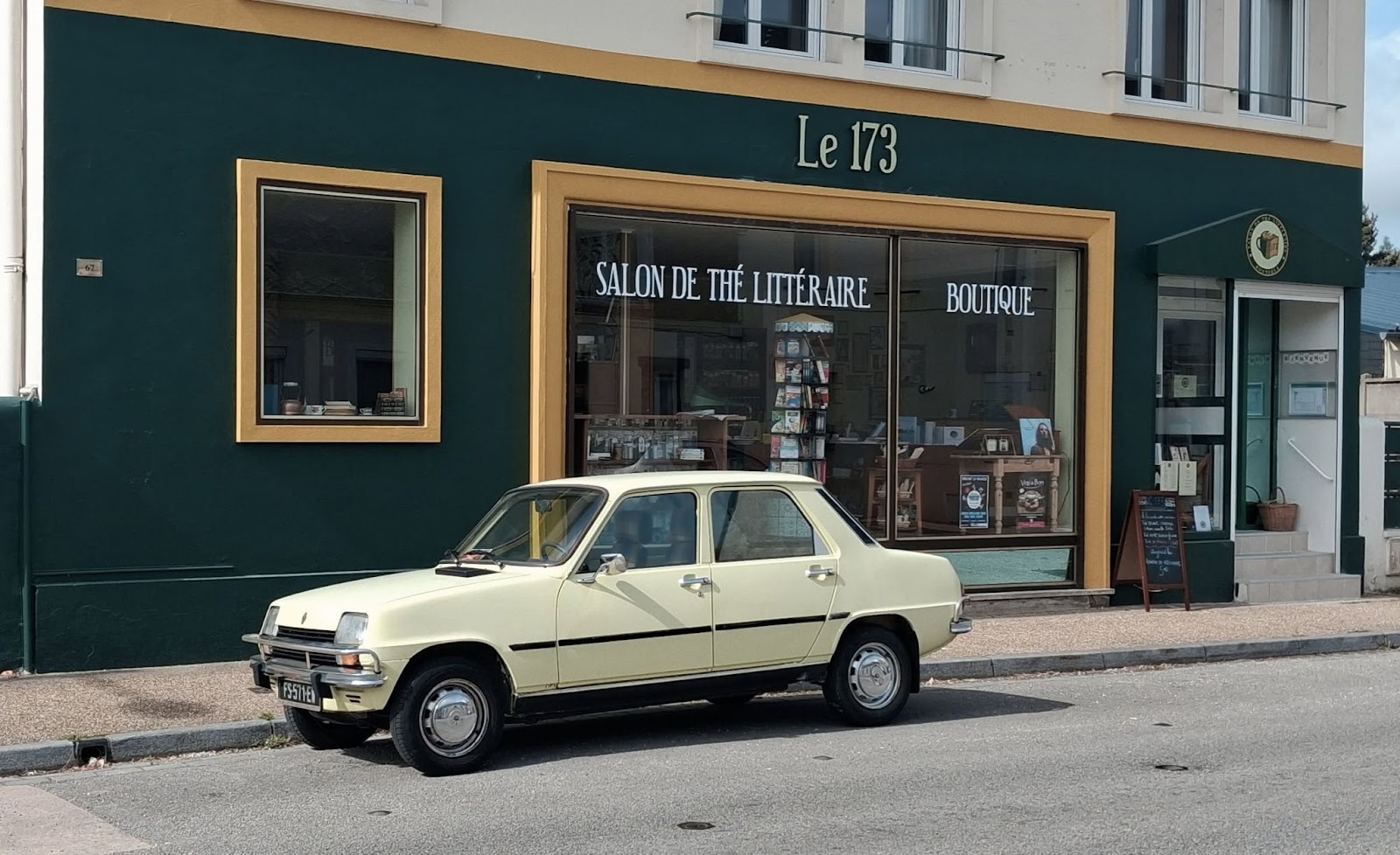 Devanture du salon de thé Le 173, avec une automobile vintage beige garée devant l'enseigne dorée.